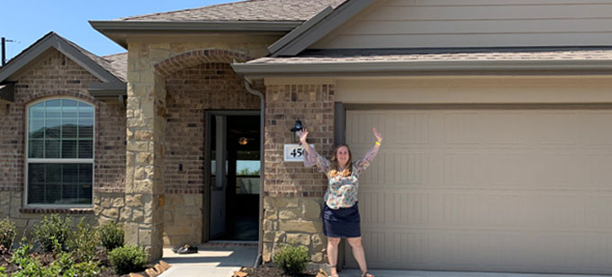 Picture of Jana Bejey from Texas standing in front of her new home with arms in air celebrating.